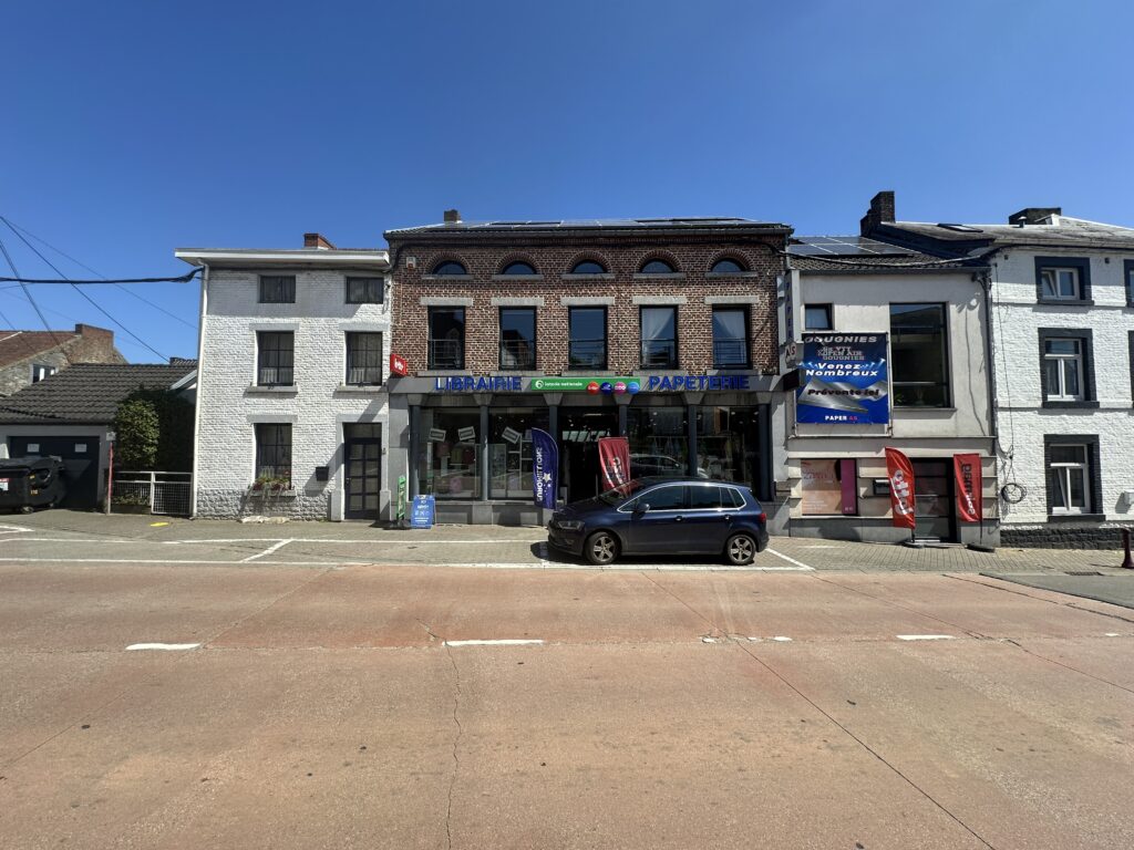 Façade de la librairie-presse Paperas à Gerpinnes, avec enseignes de librairie et papeterie visibles, sous un ciel bleu.